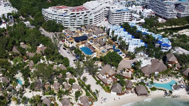 Une vue aérienne d’un complexe hôtelier comprenant plusieurs bâtiments, une plage avec des parasols et une piscine.
