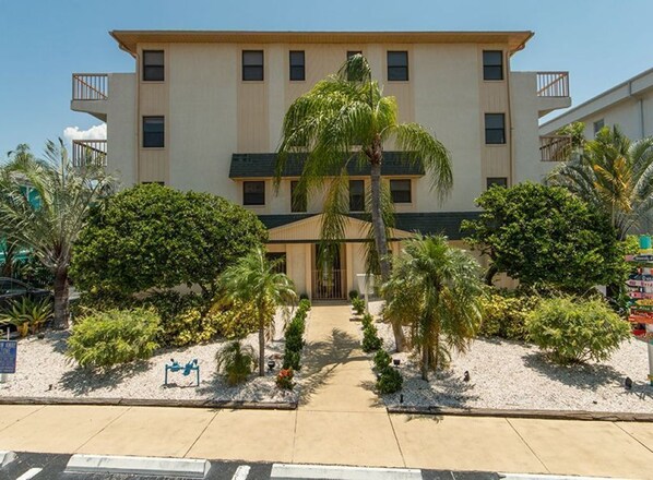 A multi-story hotel with a central entrance, surrounded by landscaped gardens and palm trees.
