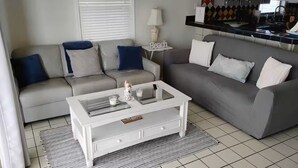 A living room with two sofas, a coffee table, and a kitchen area in the background.