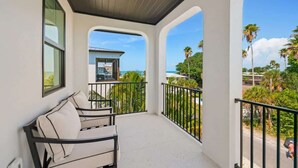 A balcony with a white exterior, a black railing, and a view of palm trees and a building across the street. - NEW! Meet Me At Sunset! 3 Homes from the Beach! (Anna Maria)