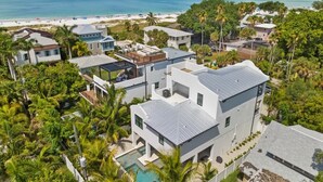 A modern multi-story residential building with a pool, surrounded by lush greenery and a beach view. - NEW! Meet Me At Sunset! 3 Homes from the Beach! (Anna Maria)