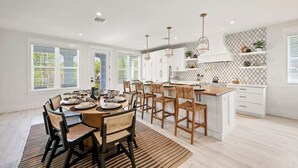 A modern kitchen with white cabinets, a wooden dining table, and a large island. - NEW! Meet Me At Sunset! 3 Homes from the Beach! (Anna Maria)