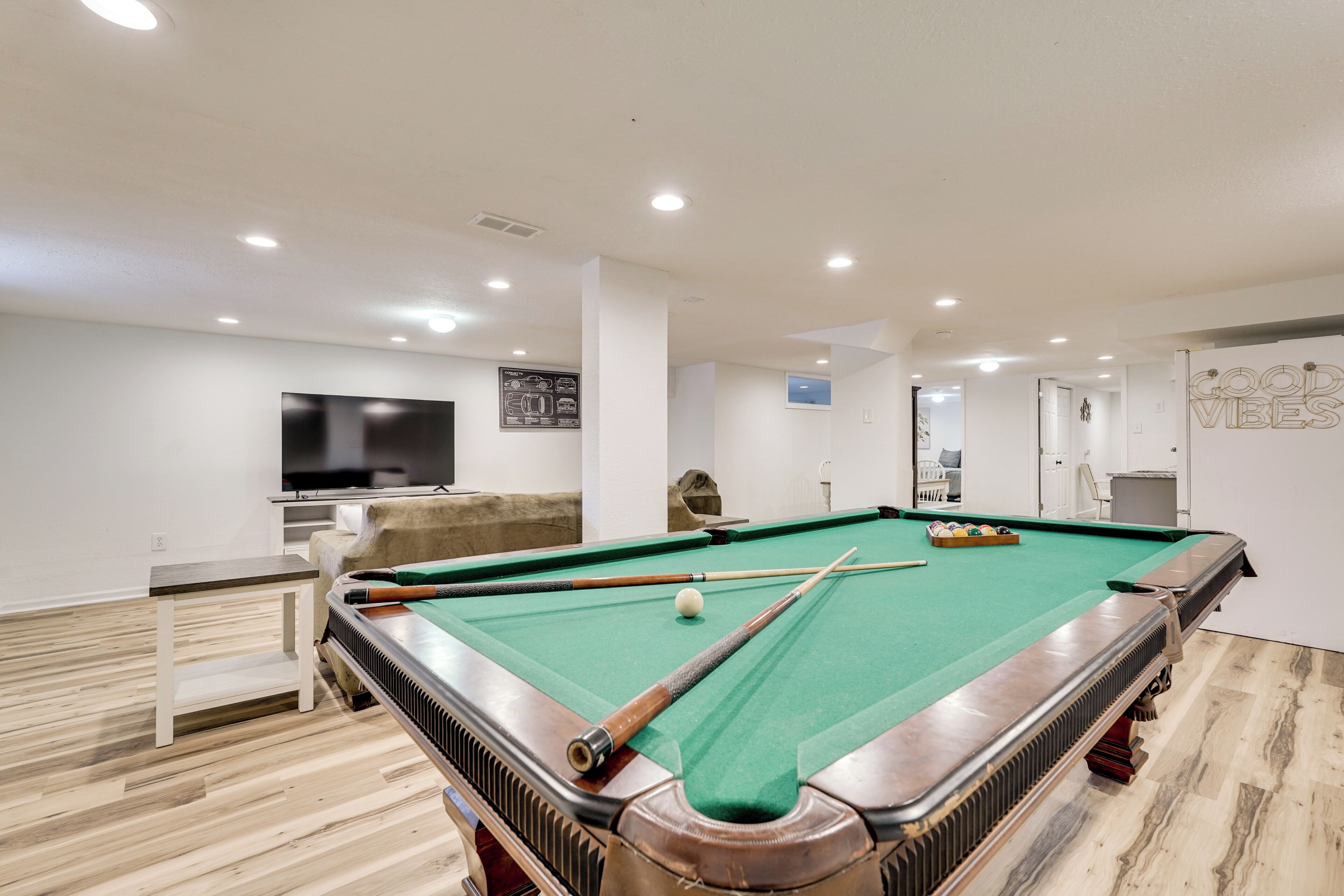 A pool table with a green felt surface, surrounded by a white wall with a mounted television.