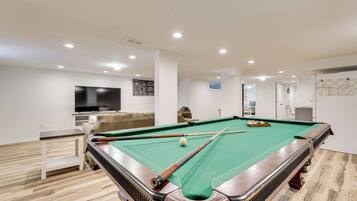 A pool table with a green felt surface, surrounded by a white wall with a mounted television.