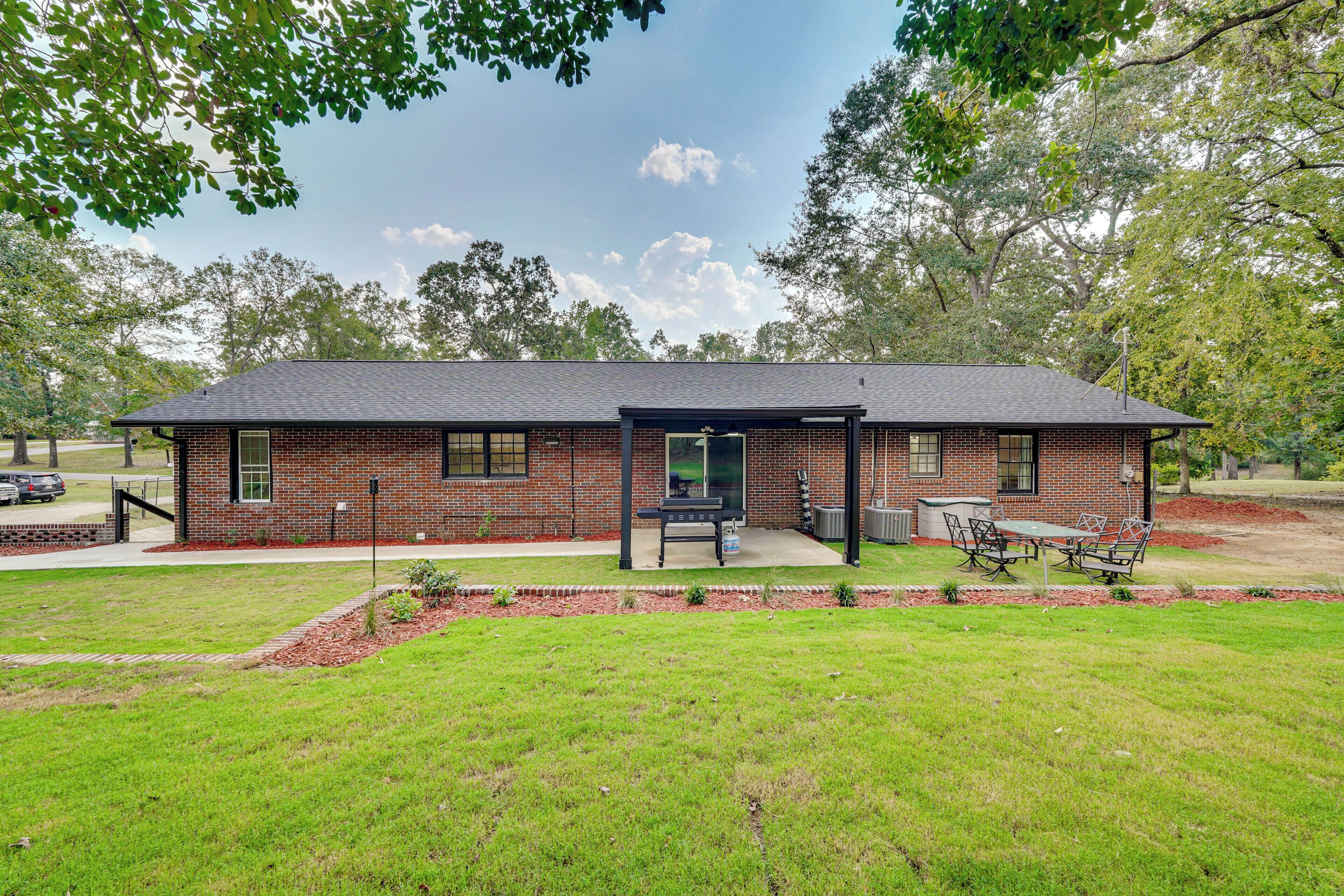 A single-story brick house with a covered patio, a lawn, and a barbecue area.