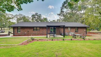 A single-story brick house with a covered patio, a lawn, and a barbecue area.