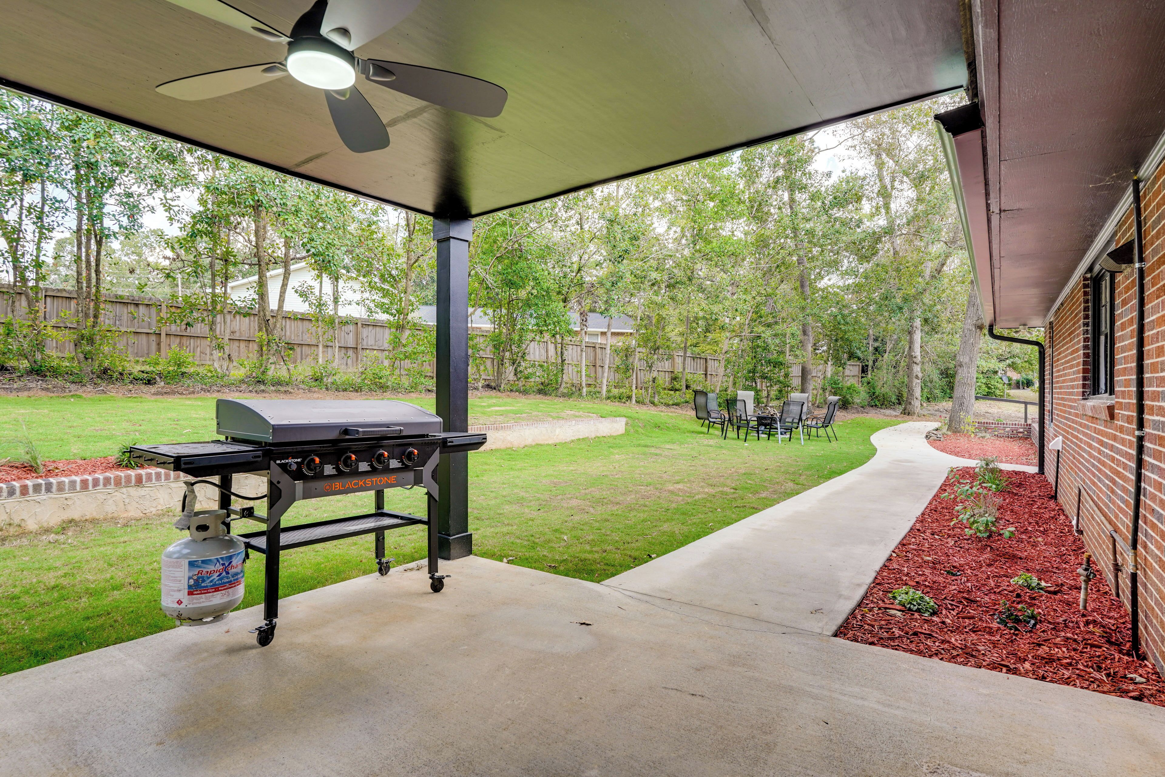 An outdoor patio with a grill, seating area, and a view of a backyard.