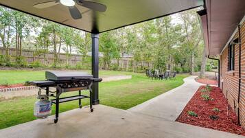 An outdoor patio with a grill, seating area, and a view of a backyard.