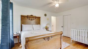 A bedroom with a wooden bed, a white crib, a ceiling fan, and a nightstand with a lamp.