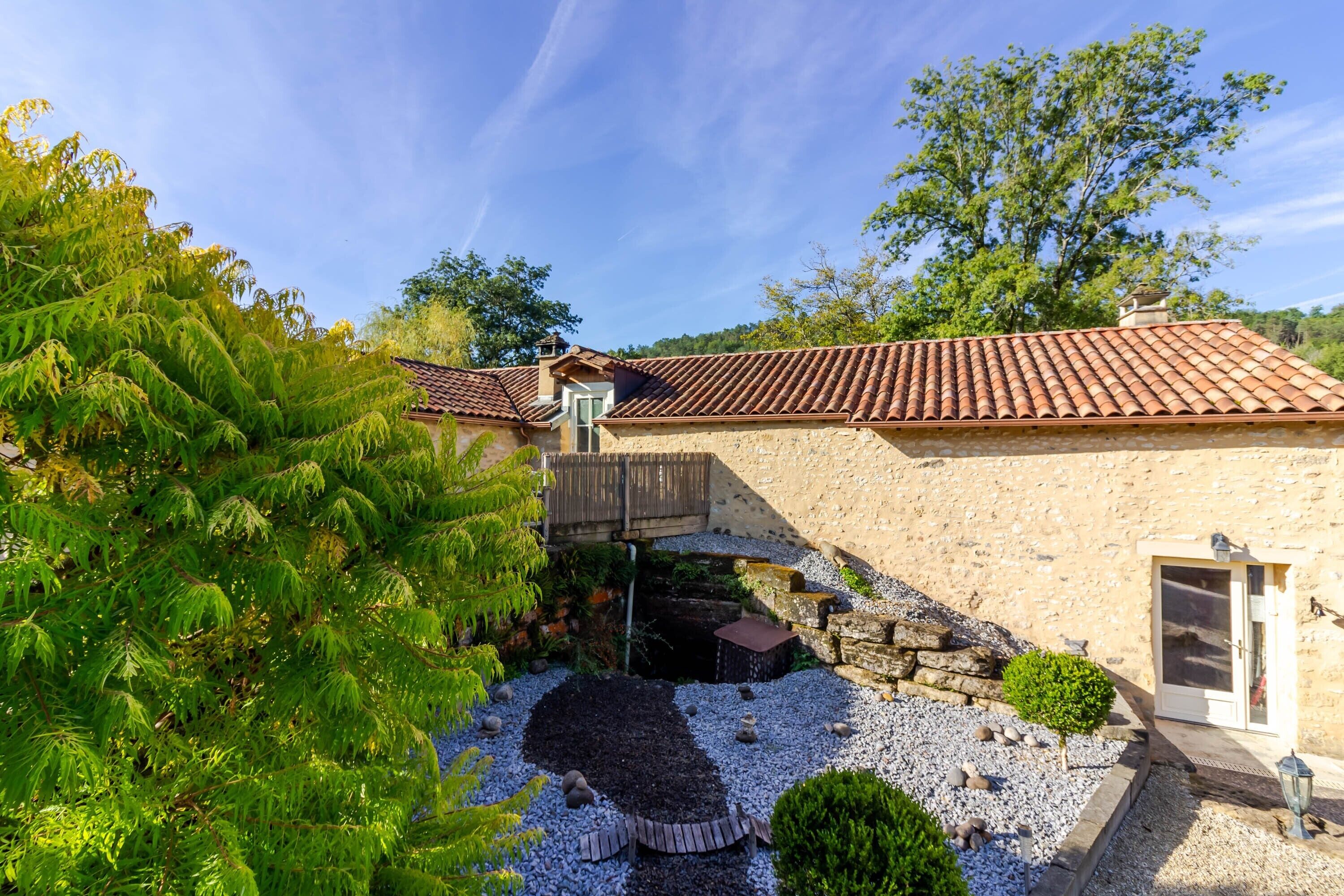 A stone building with a tiled roof, a wooden deck, and a small pond.