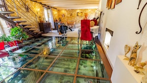 Un intérieur moderne avec un plancher en verre donnant sur un niveau inférieur, des murs en pierre, un escalier et divers éléments décoratifs.