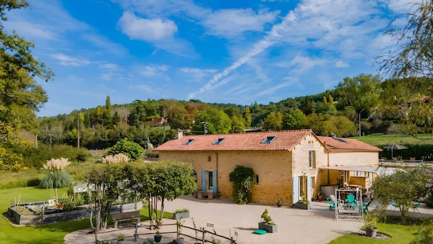 Une maison avec un toit en tuiles, une allée en gravier et un petit étang.
