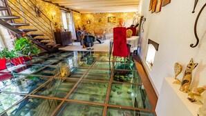Un intérieur moderne avec un plancher en verre donnant sur un niveau inférieur, des murs en pierre, un escalier et divers éléments décoratifs.