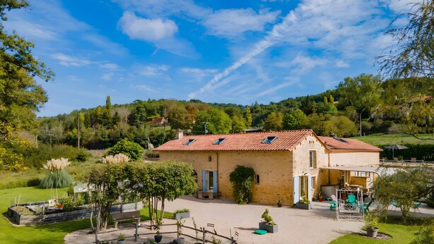 Une maison avec un toit en tuiles, une allée en gravier et un petit étang.