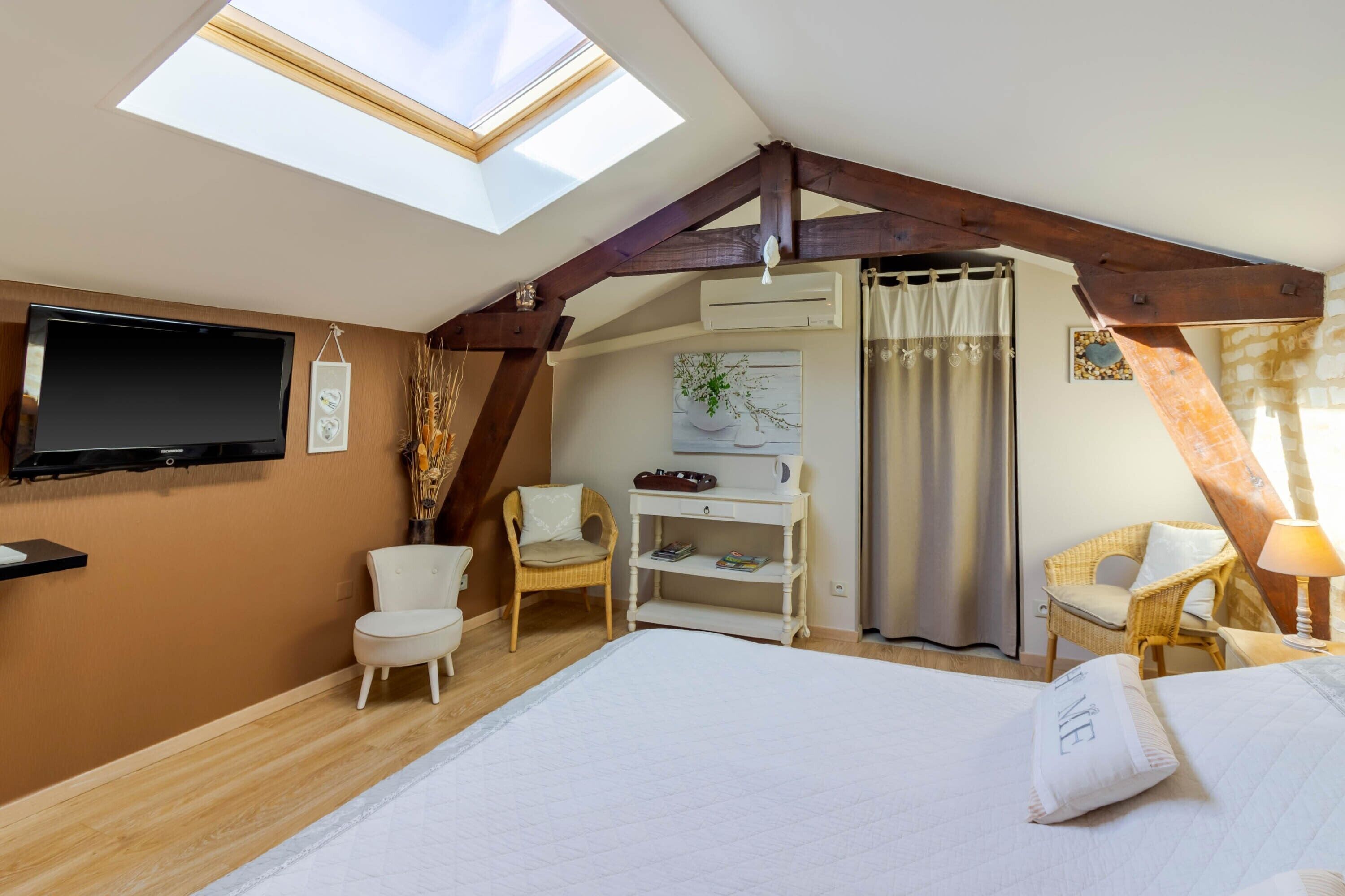 Une chambre à coucher avec un puits de lumière, un lit, une télévision, une chaise, une étagère et une fenêtre avec des rideaux.