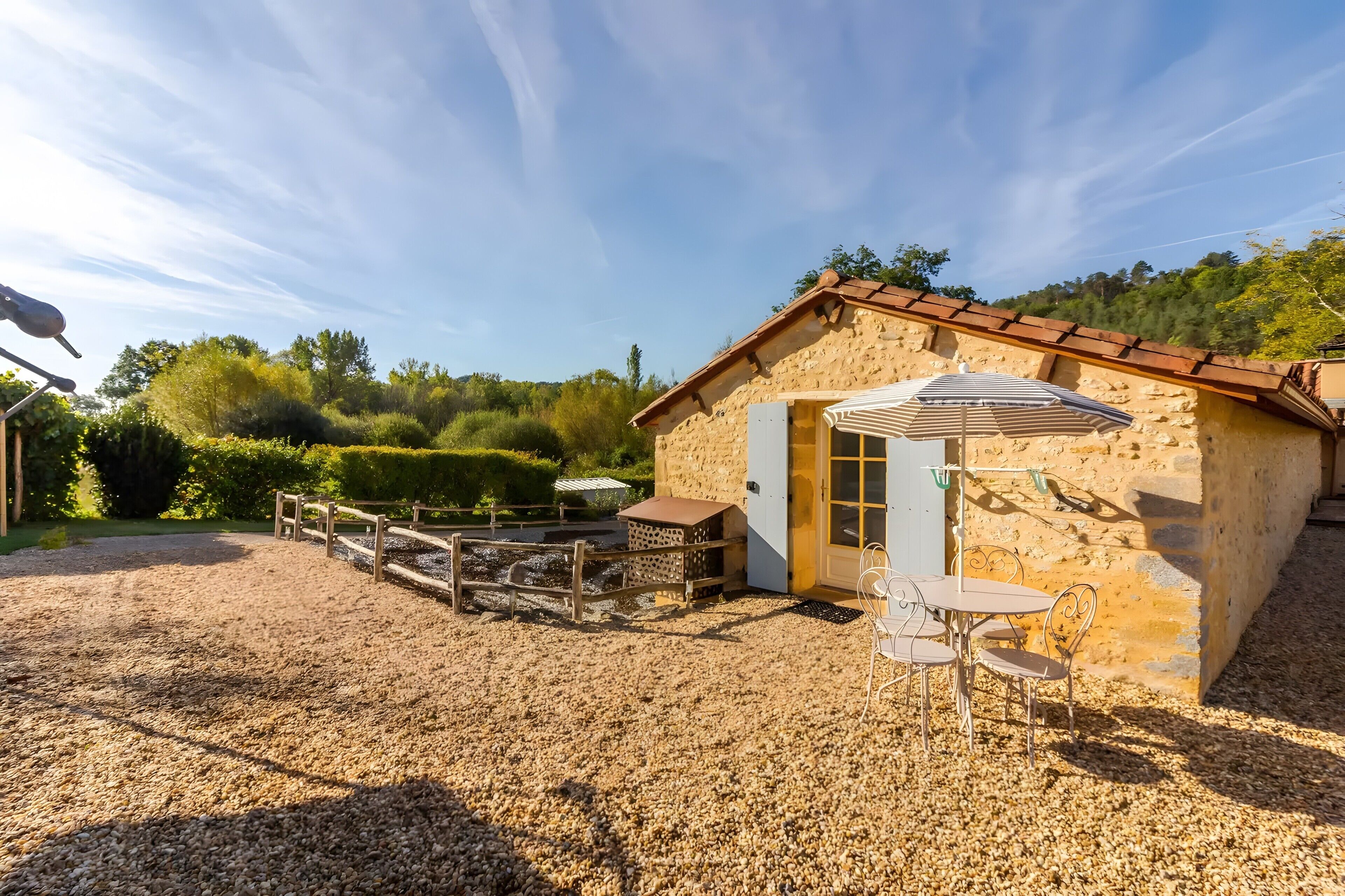 A stone building with a tiled roof, a gravel patio, and a table with chairs.