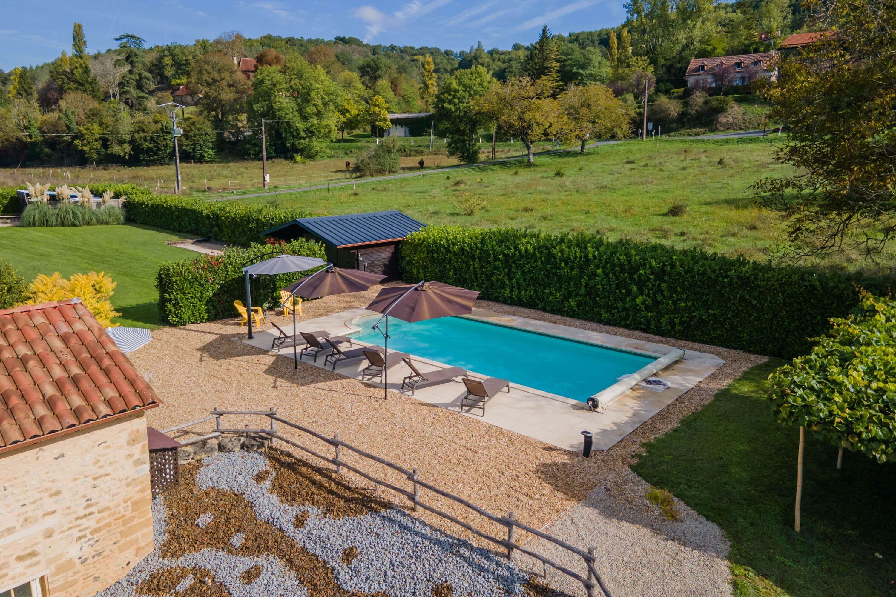 A swimming pool with lounge chairs and umbrellas, surrounded by a landscaped garden and a view of a hillside.