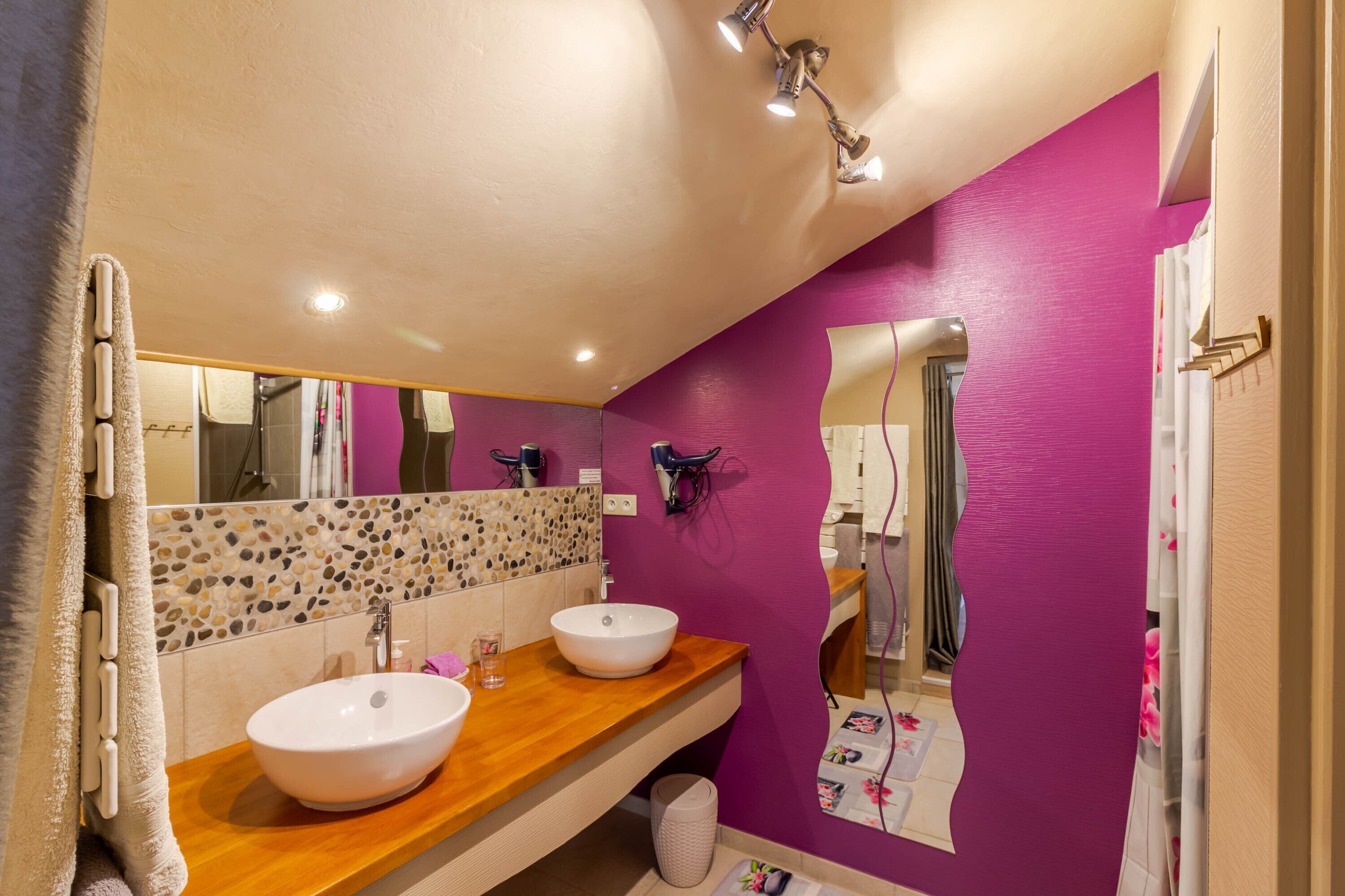 Une salle de bain avec deux lavabos, un miroir et un mur recouvert de carreaux.