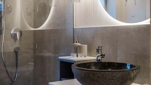 A modern bathroom with a large, dark stone sink, a glass shower enclosure, and a white countertop with a soap dispenser and glass. - Starry Loft 212 (Novale di Sotto)