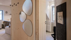 A hotel room with a wooden wall, a door with a number sign, and a view of a hallway with a desk and chair. - Starry Loft 212 (Novale di Sotto)