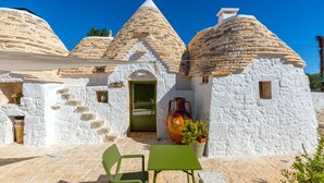 A traditional stone house with conical roofs, a door, and a table with chairs outside. - Villa 'Trulli E Frasche, Intera' with Private Pool, Wi-Fi and Air Conditioning (Martina Franca)