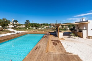 Ein Schwimmbad mit Holzterrasse, Sitzgelegenheiten im Freien und Blick auf umliegende Gebäude.