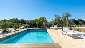 A rectangular swimming pool with a wooden deck, surrounded by lounge chairs and a grassy area with trees. - Villa 'Trulli E Frasche, Intera' with Private Pool, Wi-Fi and Air Conditioning (Martina Franca)