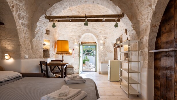 A rustic room with a bed, a wooden shelf, and a view through an arched doorway. - Villa 'Trulli E Frasche, Intera' with Private Pool, Wi-Fi and Air Conditioning (Martina Franca)