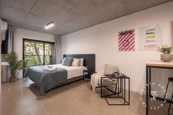 A modern bedroom with a bed, bedside table, chair, and a window with curtains. - Top Rentals Huergo (Buenos Aires)