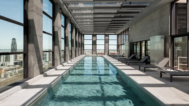 A modern indoor swimming pool with clear glass walls and a city view. - Top Rentals Huergo (Buenos Aires)
