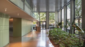 A modern indoor space with a long corridor, lockers, a reception desk, and a large window with a view of trees. - Top Rentals Huergo (Buenos Aires)