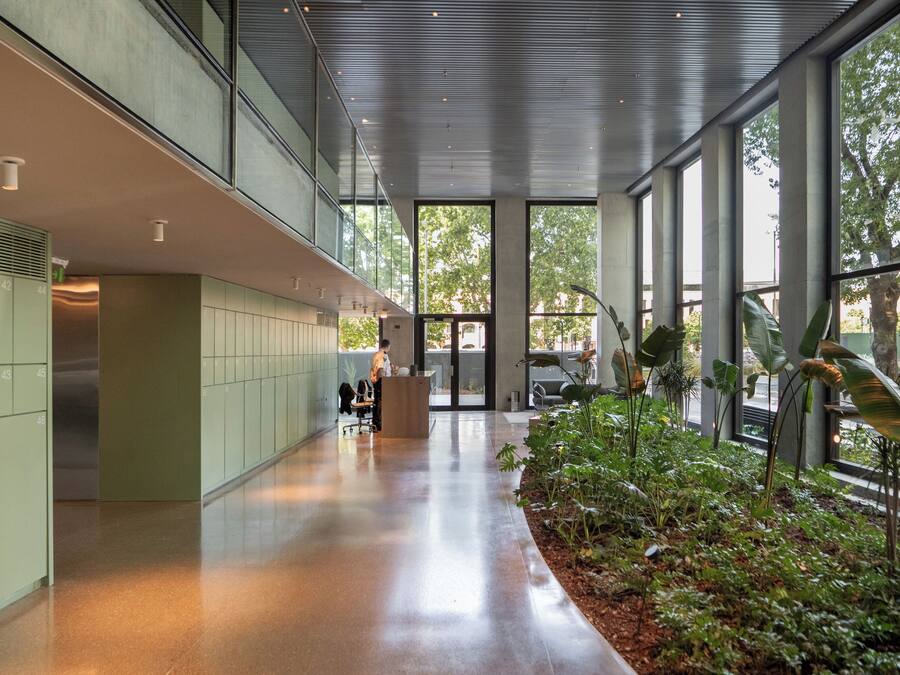 A modern indoor space with a long corridor, lockers, a reception desk, and a large window with a view of trees.