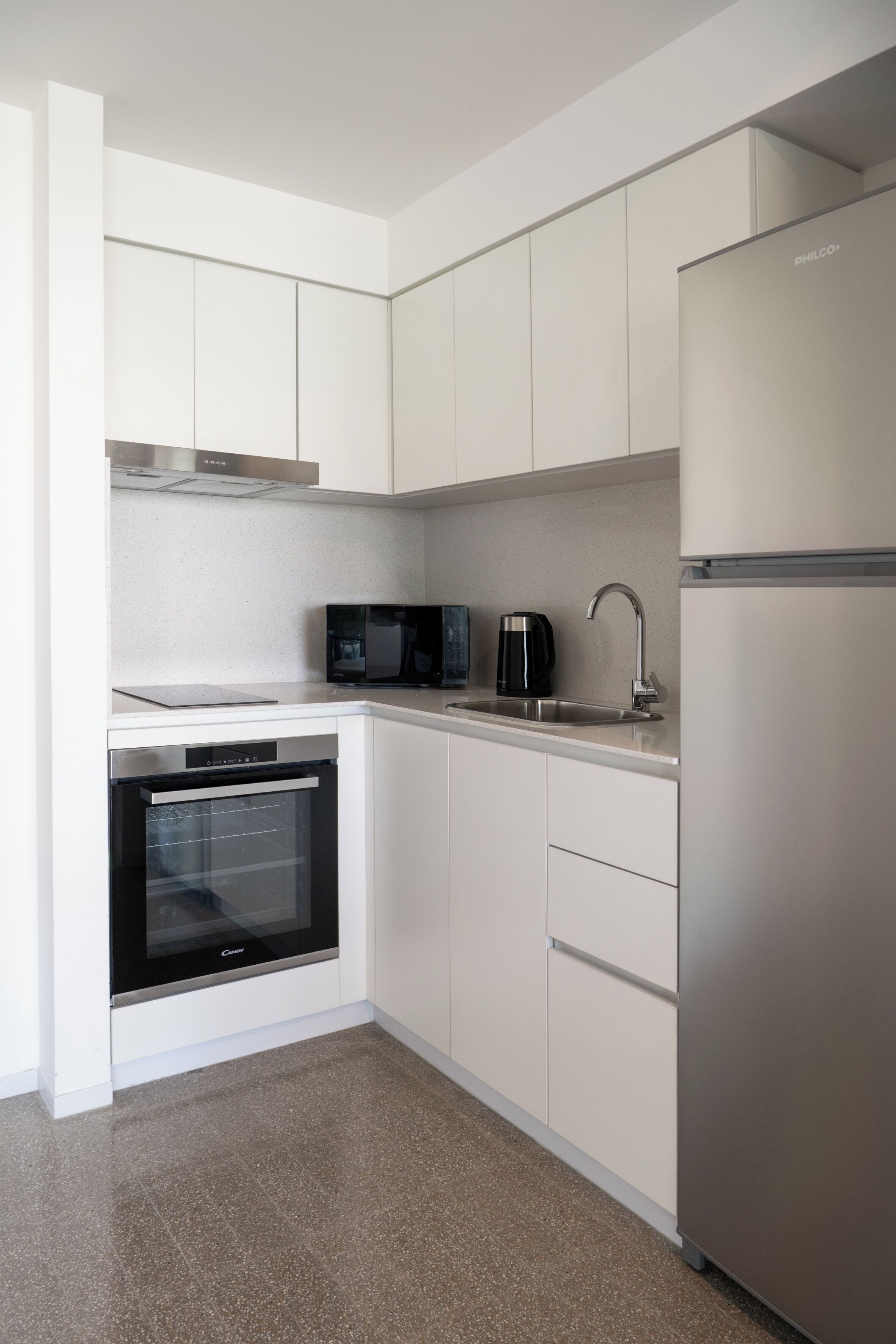Una cocina moderna con armarios blancos, horno integrado, microondas, cafetera y refrigerador de acero inoxidable.