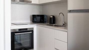 Una cocina moderna con armarios blancos, horno integrado, microondas, cafetera y refrigerador de acero inoxidable.
