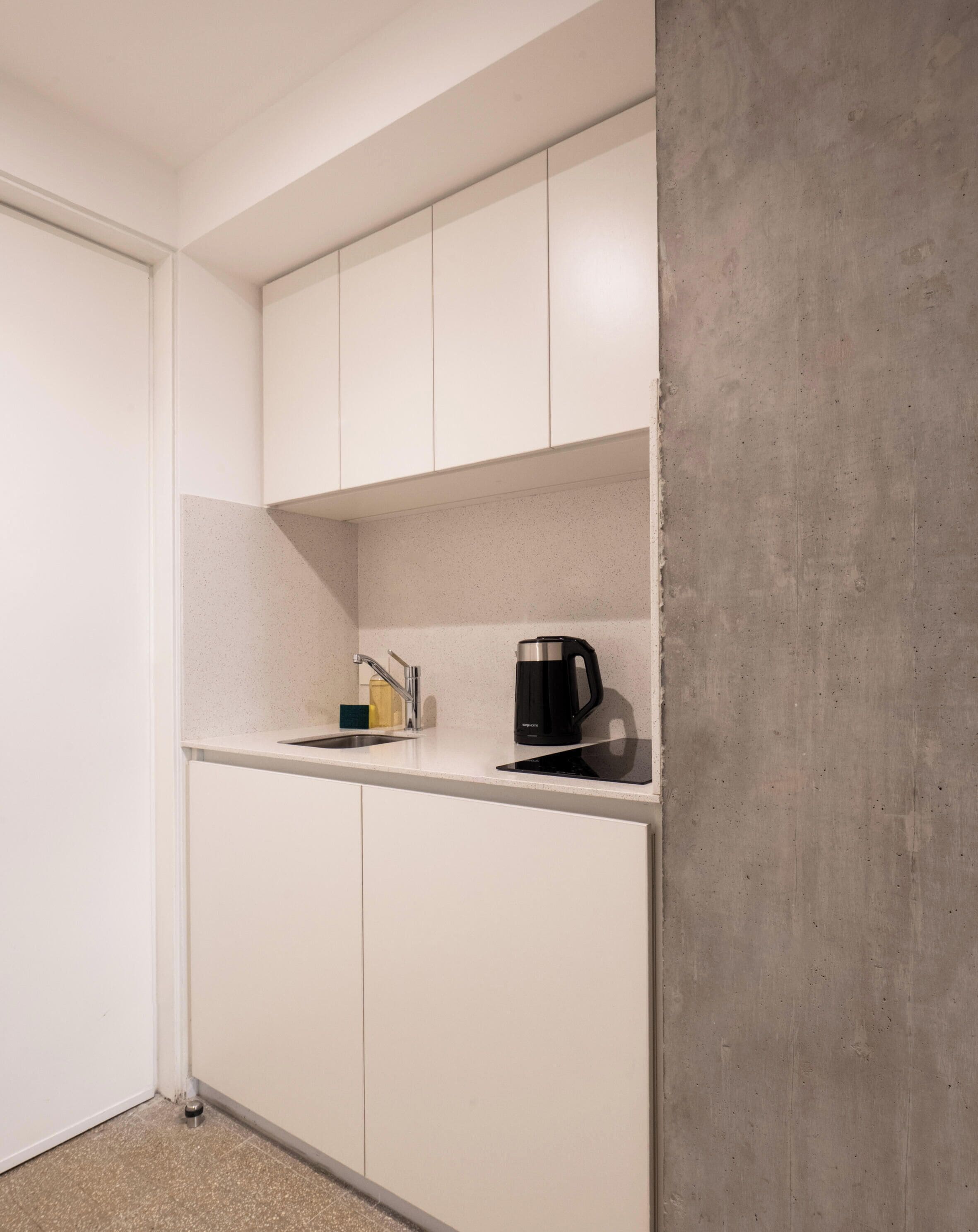 Uma cozinha compacta com armários brancos, bancada, cafeteira e dispensador de sabonete.