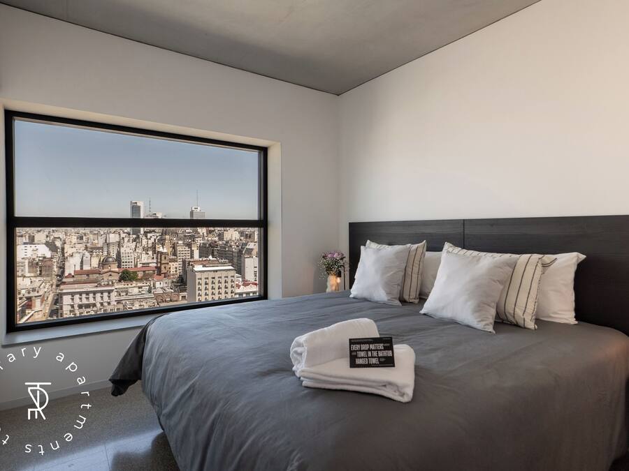 A modern hotel room with a large window, a neatly made bed, and a city view.