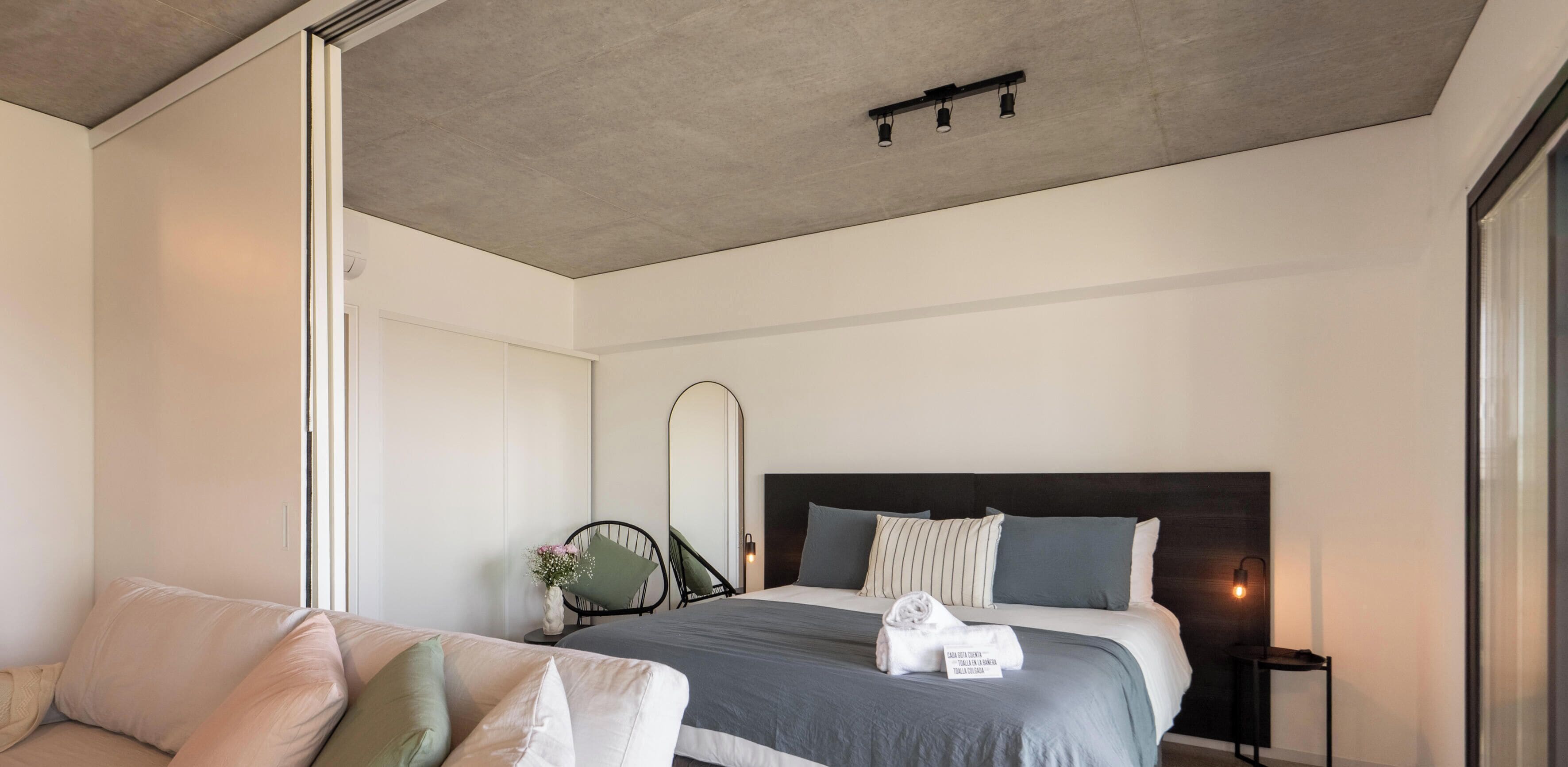 Quarto moderno com cama, mesa de cabeceira e espelho.