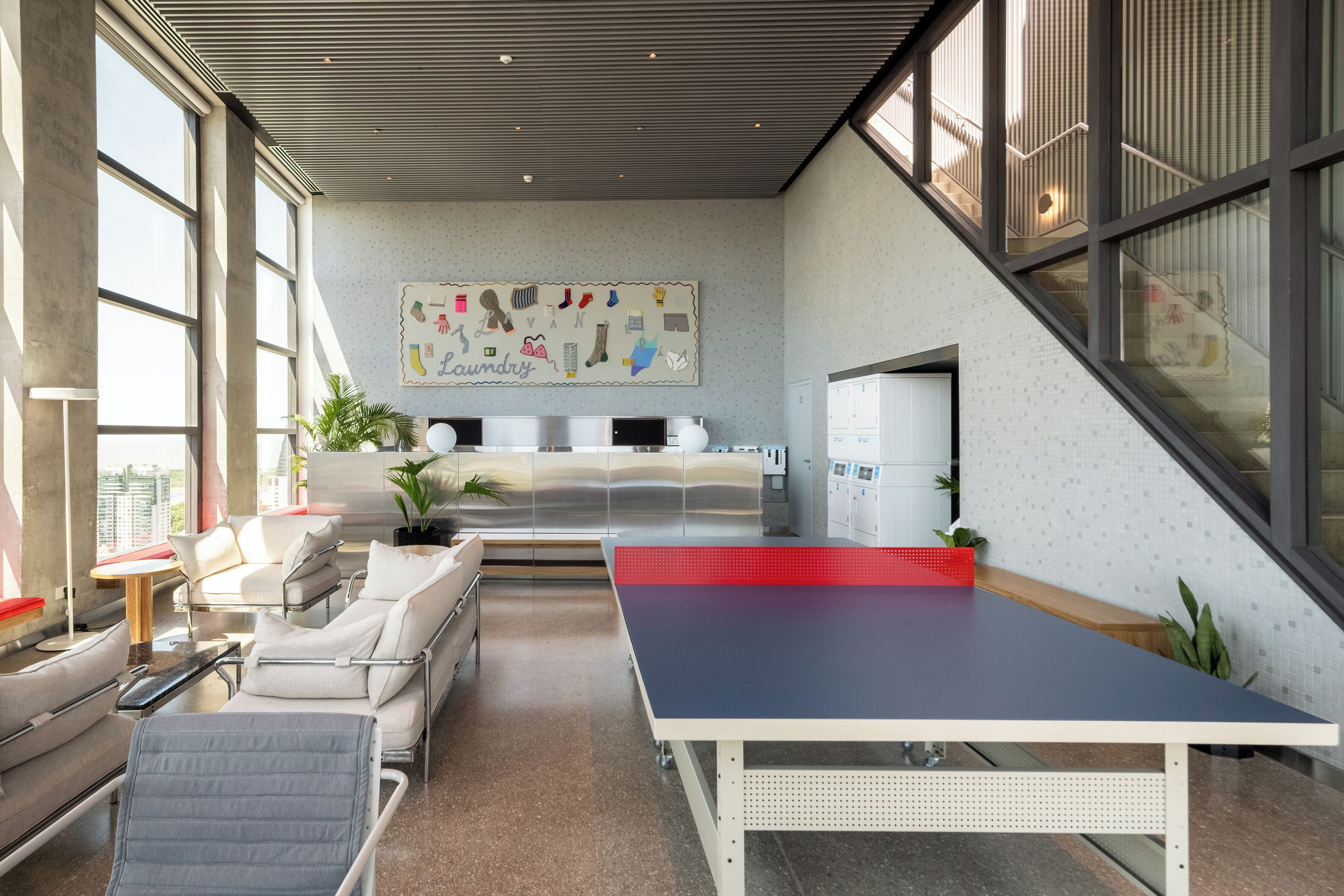 Un moderno vestíbulo de hotel con mesa de ping pong, asientos cómodos, una obra de arte grande en la pared y ventanas amplias.