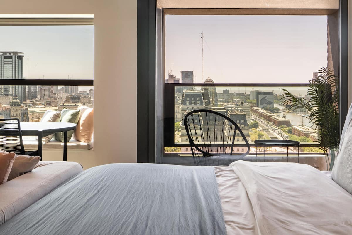 A bedroom with a large window, a bed, a chair, and a small table.