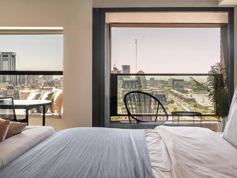 Ein Schlafzimmer mit großem Fenster, einem Bett, einem Sessel und einem kleinen Tisch.