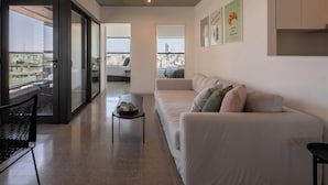 A modern living room with a white sofa, a small table, and a chair. There are large windows offering a city view. - Top Rentals Huergo (Buenos Aires)
