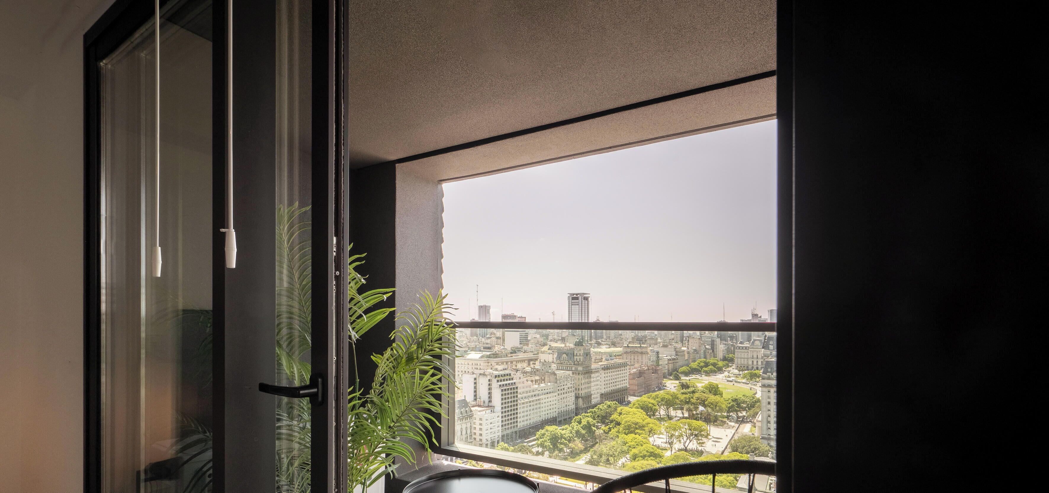 A room with a large window, a potted plant, and a view of a cityscape.
