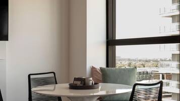 A modern room with a round table, two black chairs, a window with a view of buildings, and a white wall.