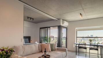 A modern living room with a sofa, a dining table, and a large window offering a city view.