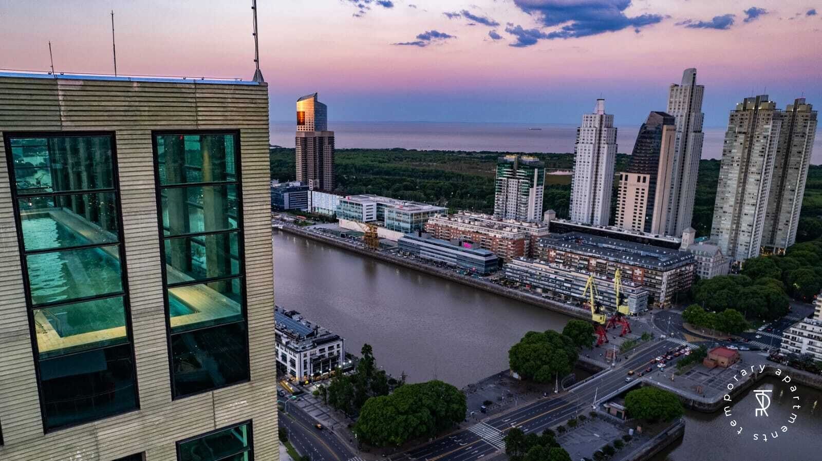 Een modern gebouw met grote ramen met uitzicht op een rivier en een stadsbeeld met hoogbouw.