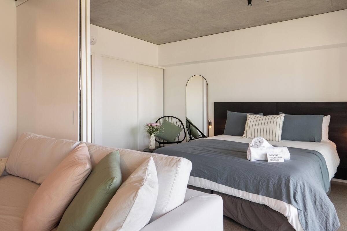 A hotel room with a bed, a sofa, a mirror, and a small table with a vase of flowers.