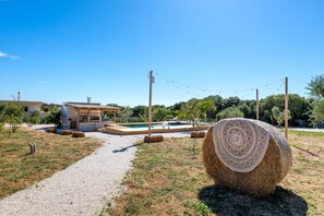 A rural property with a swimming pool, hay bales, and a clear sky.