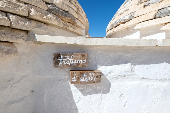 Un mur de pierre sur lequel sont fixées deux enseignes en bois, l’une portant l’inscription « Profumo » et l’autre « di stelle ».