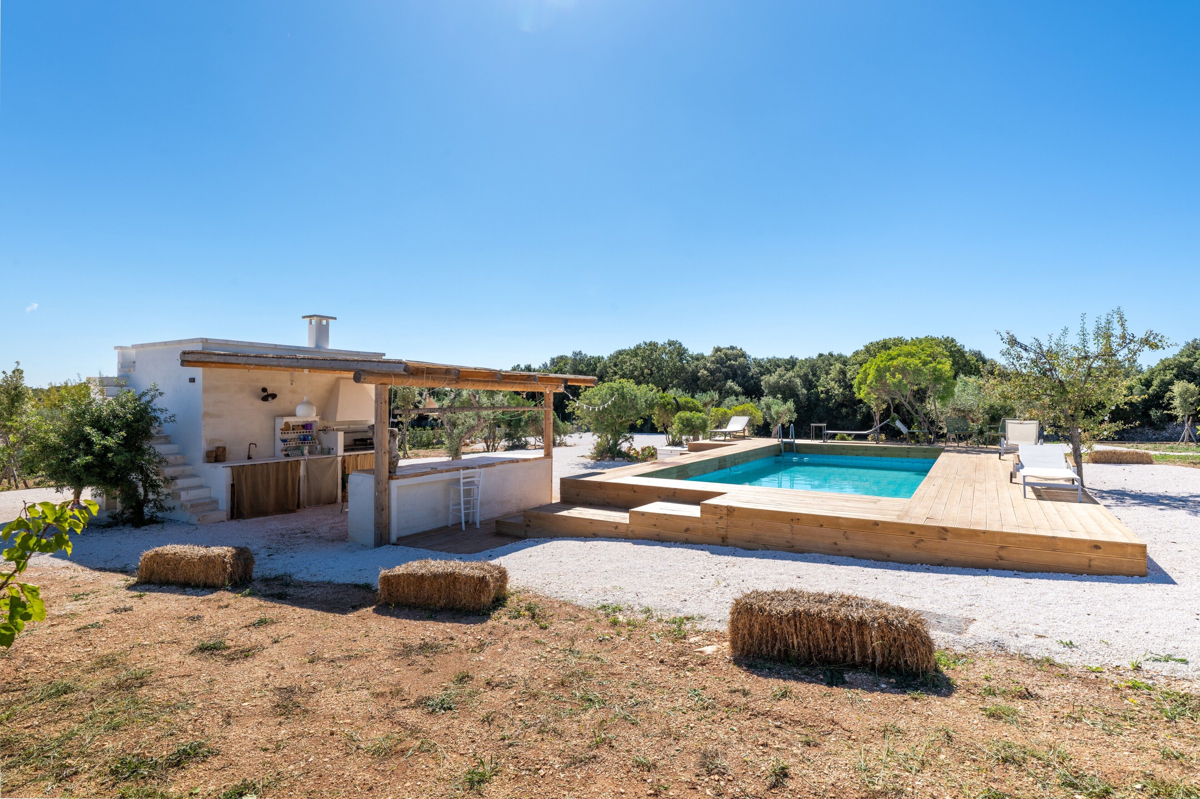 Un espace piscine extérieur moderne, doté d’une terrasse en bois, d’un petit bâtiment agrémenté d’une pergola et de bottes de foin.