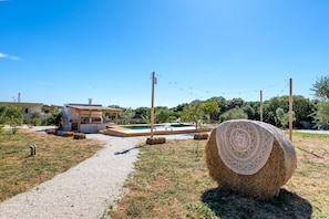 A rural property with a swimming pool, hay bales, and a clear sky.